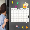 A magnetic dry erase monthly planner calendar is displayed on a refrigerator door with colorful markers.