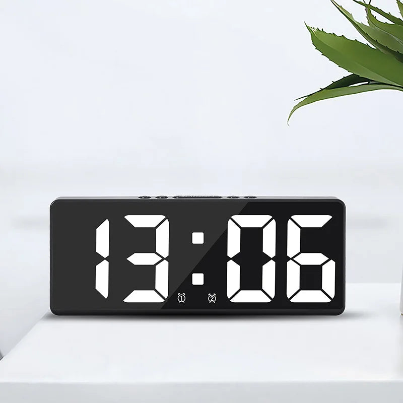 A black digital alarm clock displaying the time 13:06 on a white surface.
