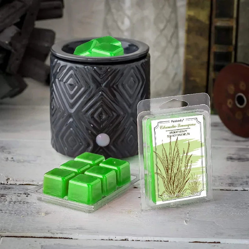Green wax melt molds and a dark ceramic container are displayed on a white wooden surface.