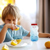A young child is eating lemon slices while a glass jar filled with blue ice water shaped like a snowman sits on the table.