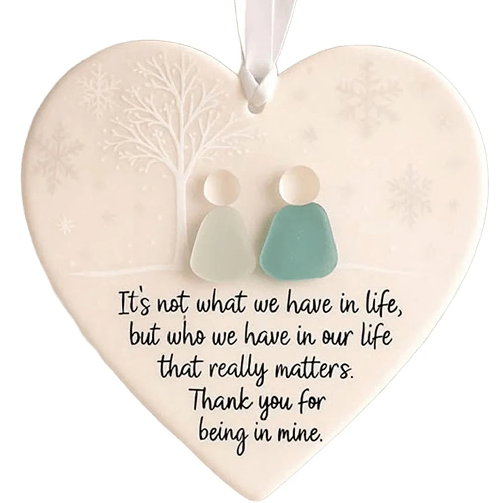 A heart-shaped sea glass Christmas ornament with a white pendant featuring a tree and snowflakes on a pale background.