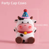 A cute white cow cake topper with a purple conical party hat and brown accents.