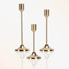 A set of three modern brass tapered candle holders with reflective glass bases.