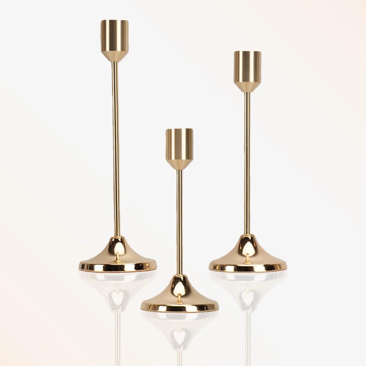 A set of three modern brass tapered candle holders with reflective glass bases.