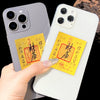 A hand holds a smartphone displaying a gold and red traditional Chinese character amulet sticker on the back.