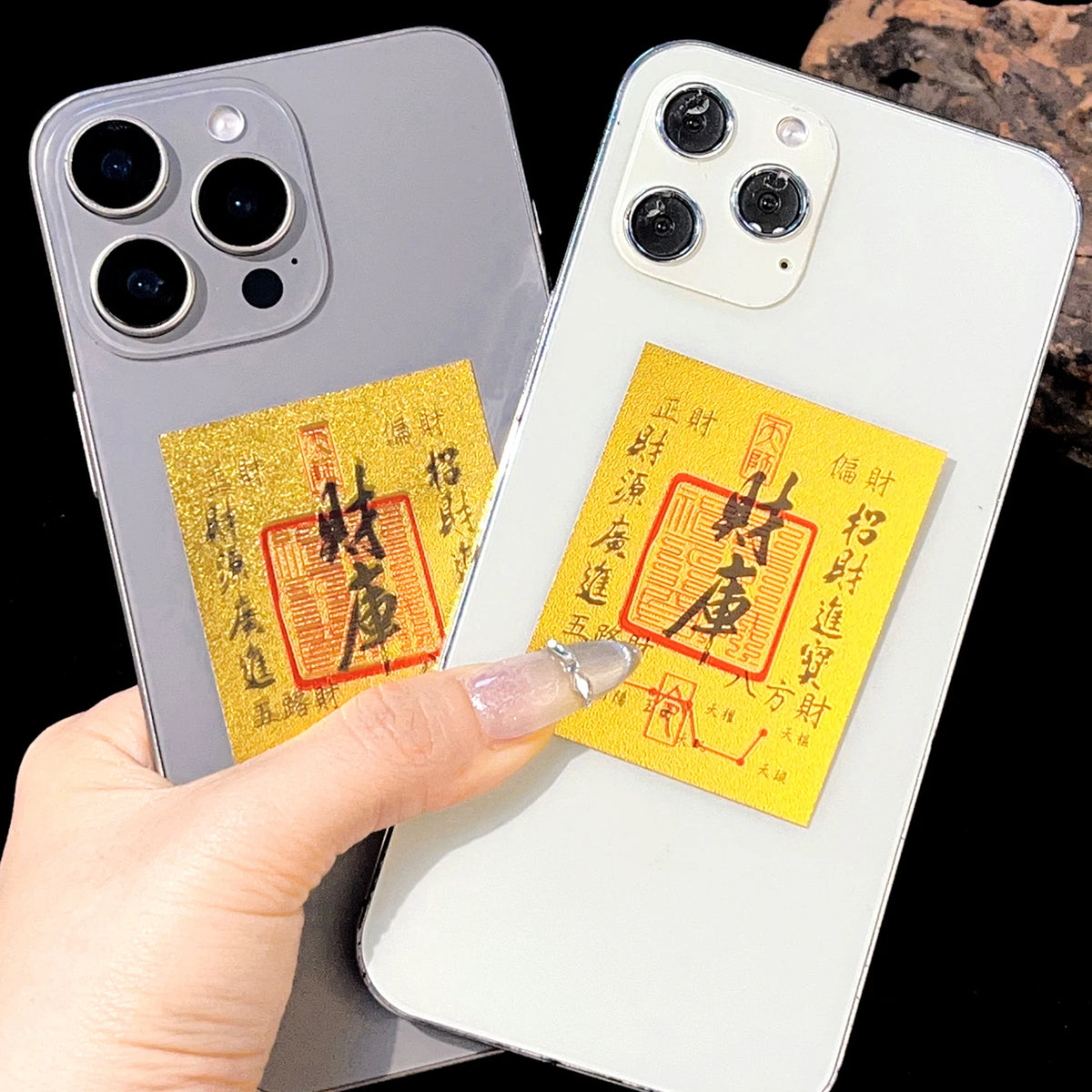 A hand holds a smartphone displaying a gold and red traditional Chinese character amulet sticker on the back.