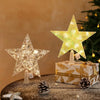 A sparkling LED Christmas tree star topper with a warm white glow resting on a gift box surrounded by pine cones.