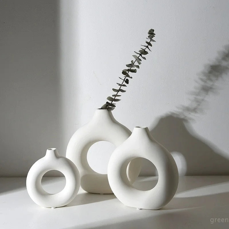 White ceramic vase with a donut pattern and a sprig of greenery on a white surface.