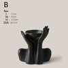A black ceramic figural vase shaped like an artistic human hand or arm.