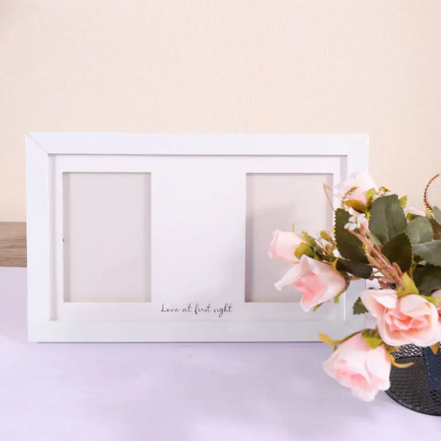 A white wooden frame with two recessed squares and the text Love at first sight, decorated with pink roses.