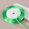 A spool of bright green satin ribbon lying on a white surface.