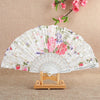 A white silk flower folding fan with pink and purple floral patterns displayed on a wooden stand.
