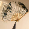 A folding hand fan with a leopard print design and a black handle is shown open against a light background.