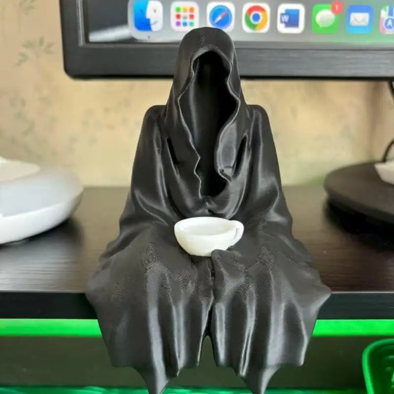 A black resin statue of a Halloween ghost draped in fabric, holding a white tea cup.