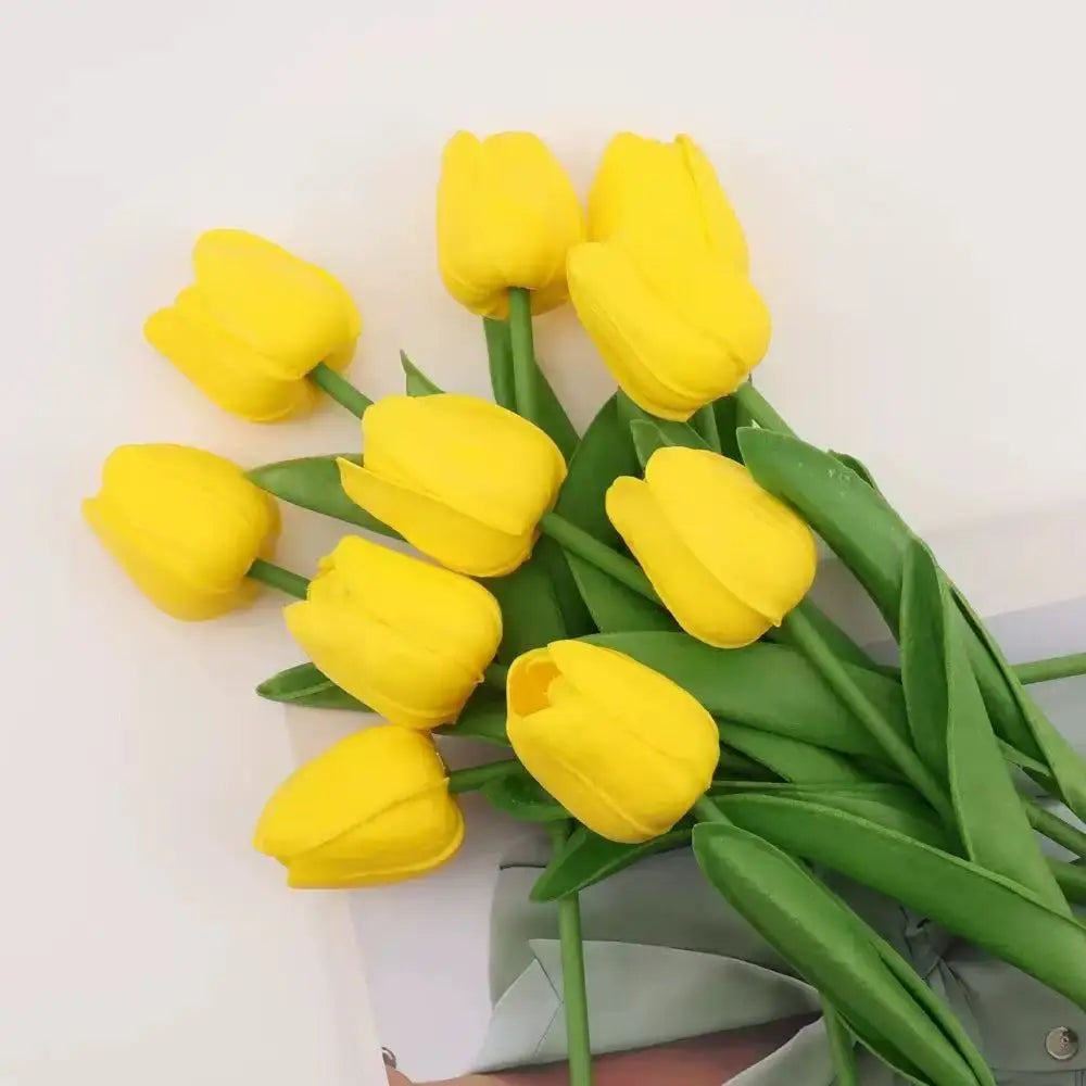A bouquet of bright yellow artificial tulips with green stems and leaves.