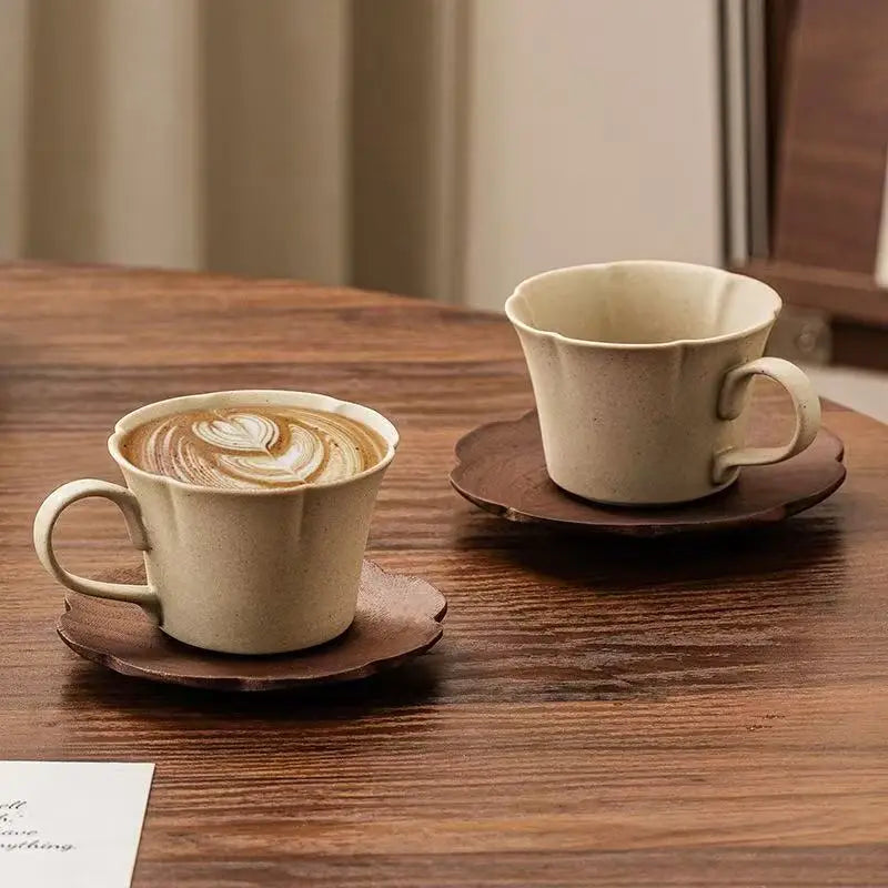 A light beige ceramic coffee cup and saucer set with latte art resting on a dark wooden table.