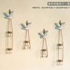 Three decorative glass terrariums featuring blue and white bird-like figures on wooden hangers.