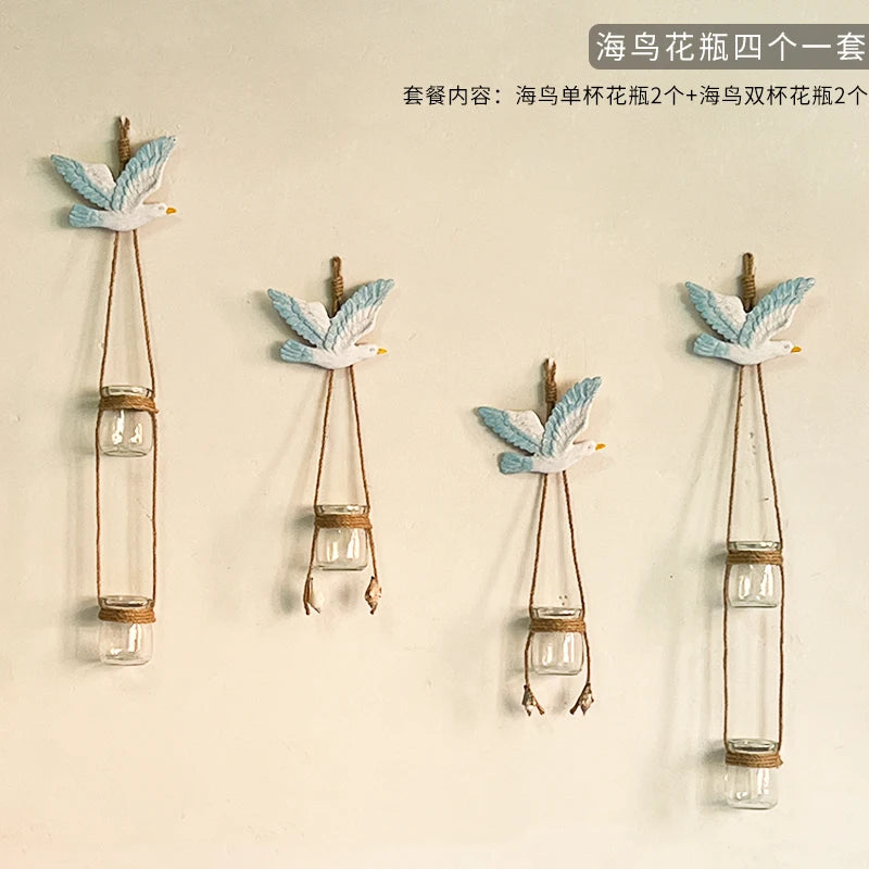 Three decorative glass terrariums featuring blue and white bird-like figures on wooden hangers.