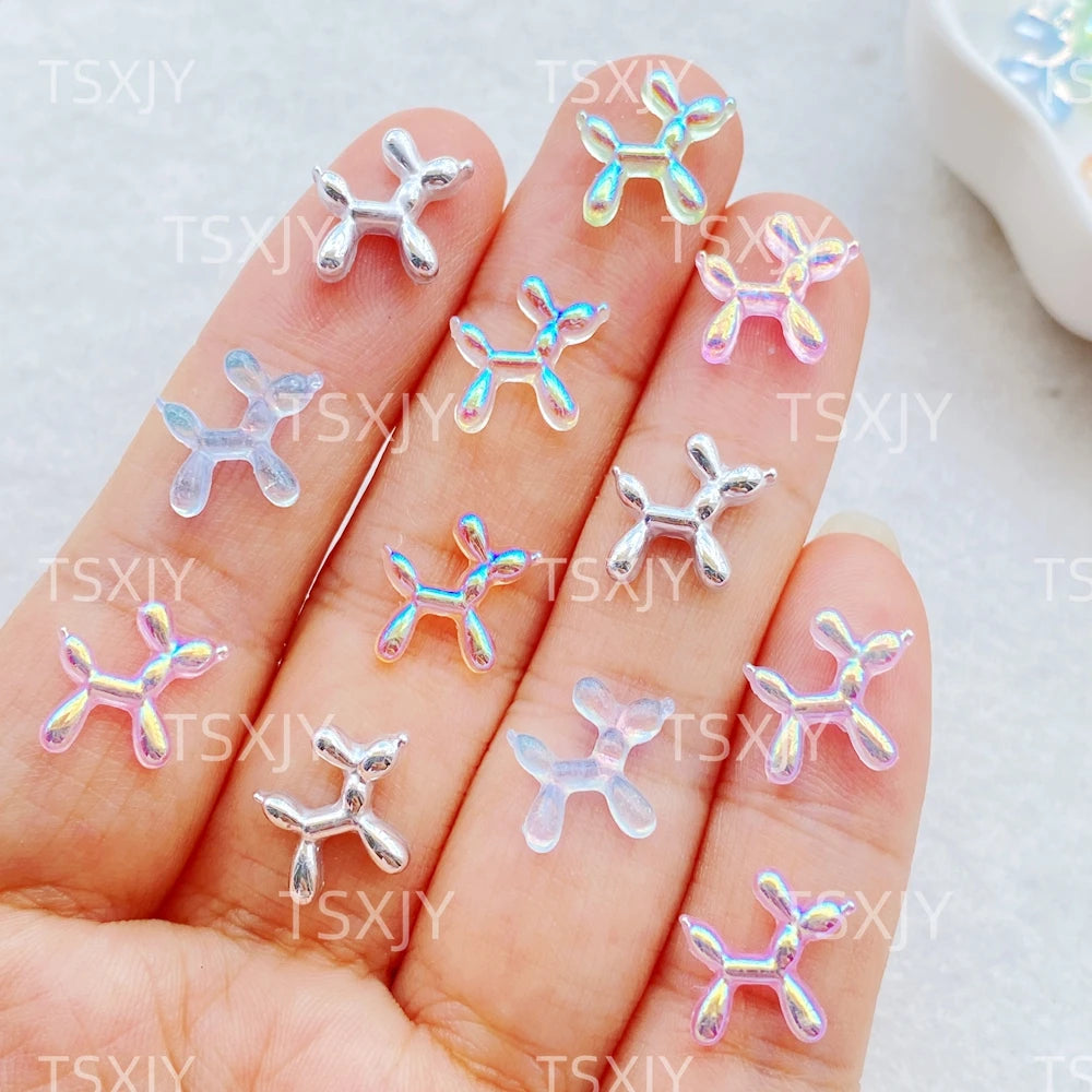 A hand displays various clear and pastel colored balloon puppy nail art charms.