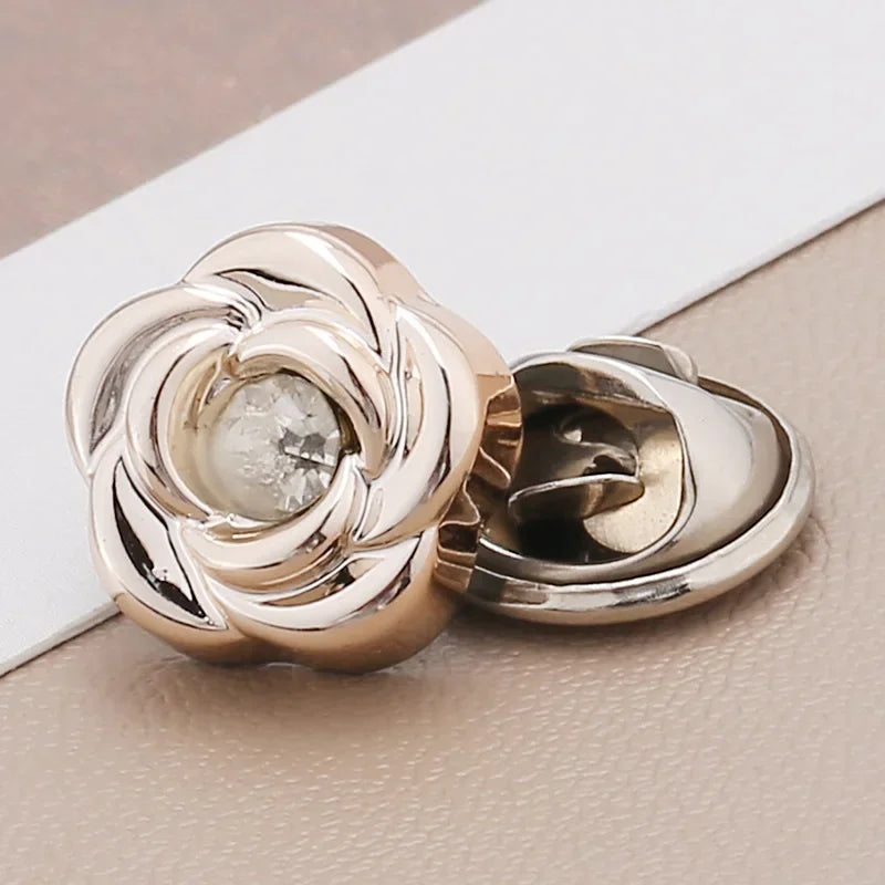 A close-up of a gold-toned, flower-shaped rhinestone brooch button with a clear stone, resting on a light surface.