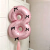 A pink foil balloon set shaped like the number 8 with black bows, hanging on a white door.
