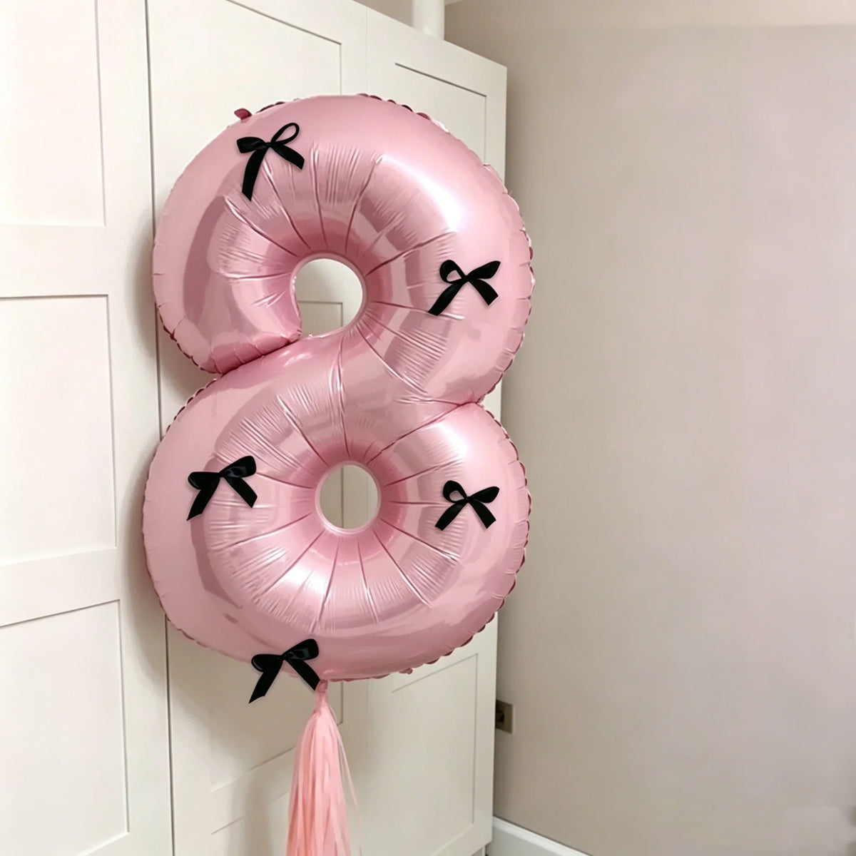 A pink foil balloon set shaped like the number 8 with black bows, hanging on a white door.
