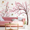 Pink cherry blossom tree wall stickers decorating a white room with a pink sofa and wooden table.