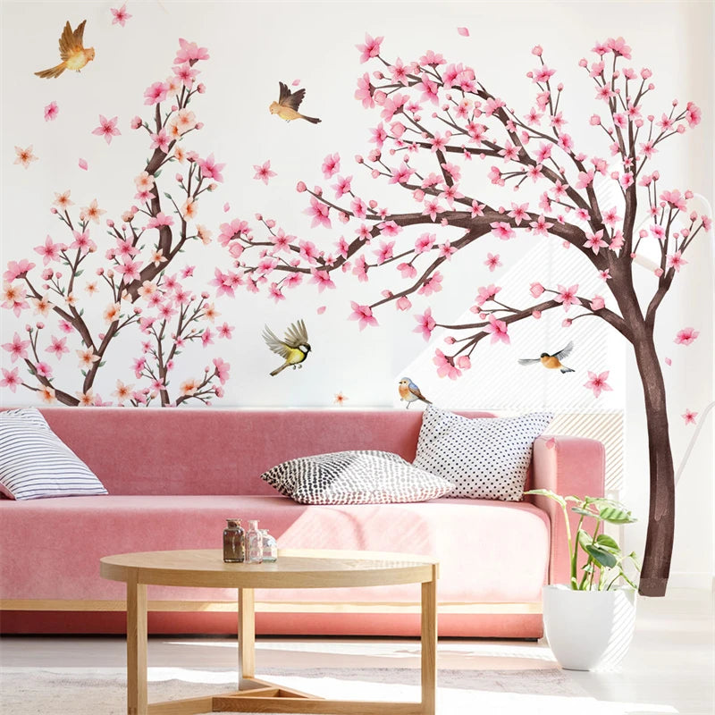 Pink cherry blossom tree wall stickers decorating a white room with a pink sofa and wooden table.