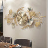 A decorative wall clock featuring a metal design of ginkgo leaves and branches on a light beige wall.
