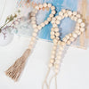 A beige beaded garland with a jute tassel is displayed on a light blue painted wooden surface.