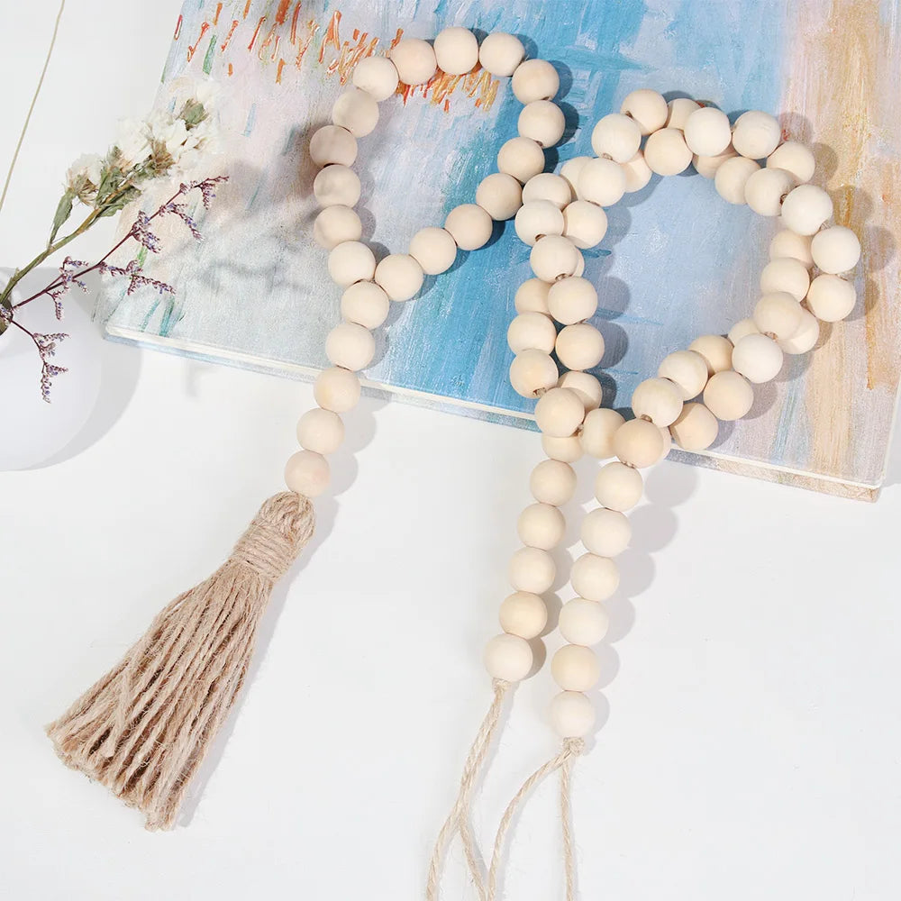 A beige beaded garland with a jute tassel is displayed on a light blue painted wooden surface.