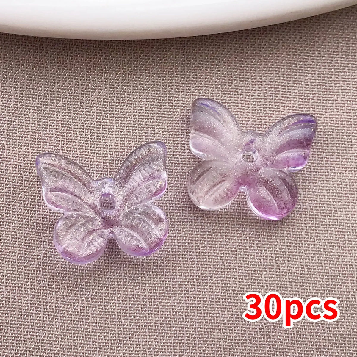 Una pequeña selección de cuentas de mariposa de vidrio iridiscente morado esparcidas sobre una superficie de tela gris.
