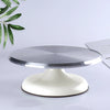 A silver aluminum cake turntable with a white base is shown on a light surface.