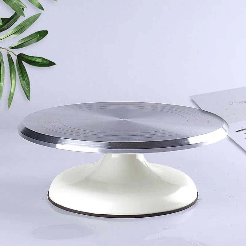 A silver aluminum cake turntable with a white base is shown on a light surface.