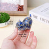 A hand holds a natural crystal cat statue with blue and gold inclusions, showing its size.