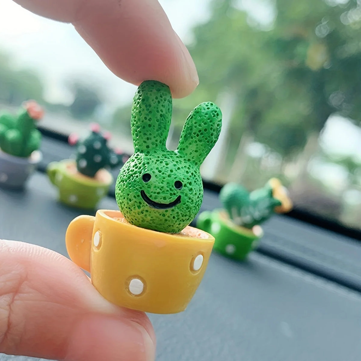 A hand holds a small, bright green resin cactus succulent in a yellow pot for home decor.