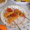A plate of golden-fried food skewers with orange and red sauces on a white polka dot plate.