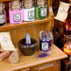 A collection of colorful glitter powders and jars displayed on a wooden shelf with parchment labels.