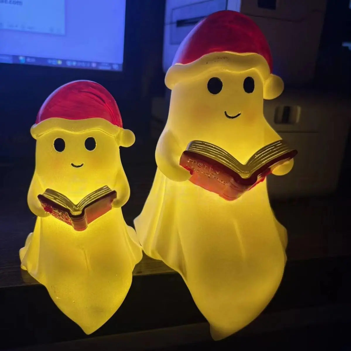 A cute ghost night light shaped like a figure reading a book, glowing yellow and pink.
