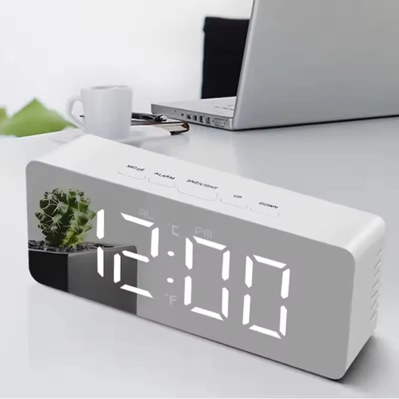 A white LED digital alarm clock displaying 12:00 with temperature and time settings on a white desk.