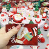 A hand holds a red festive card featuring illustrations of Santa Claus and snowmen figurines for Christmas decor.