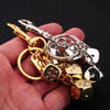 A hand holds a golden dice keychain with various charms and silver chains.