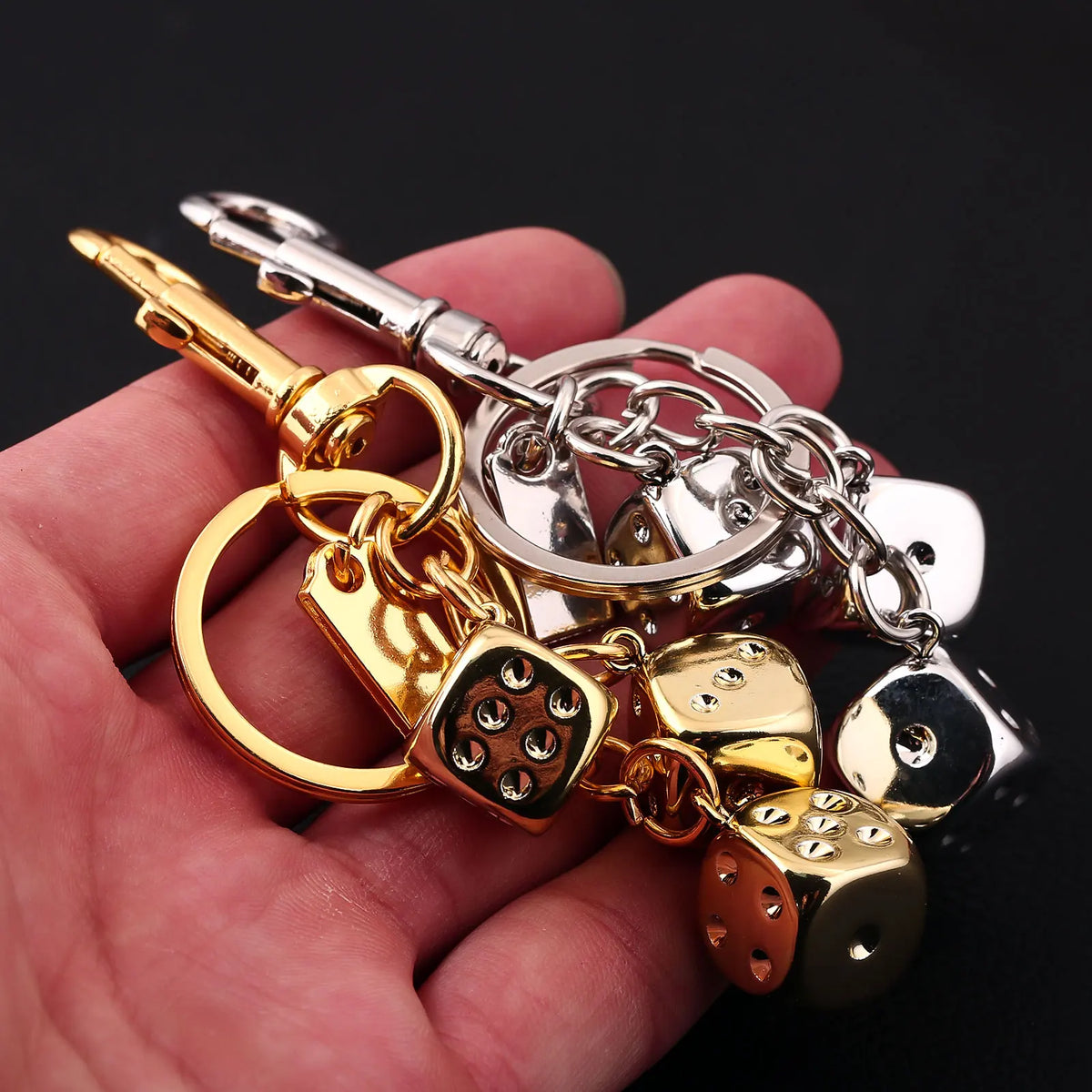 A hand holds a golden dice keychain with various charms and silver chains.
