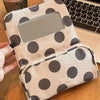 A beige canvas travel makeup bag with dark polka dots and a clear mirror, resting on a wooden surface.