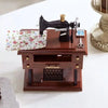 A miniature black sewing machine with a brass nozzle and a wooden box is displayed on a white surface.