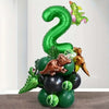 A green foil balloon shaped like the number 2 with a small dinosaur figure on top, surrounded by various green and brown ball