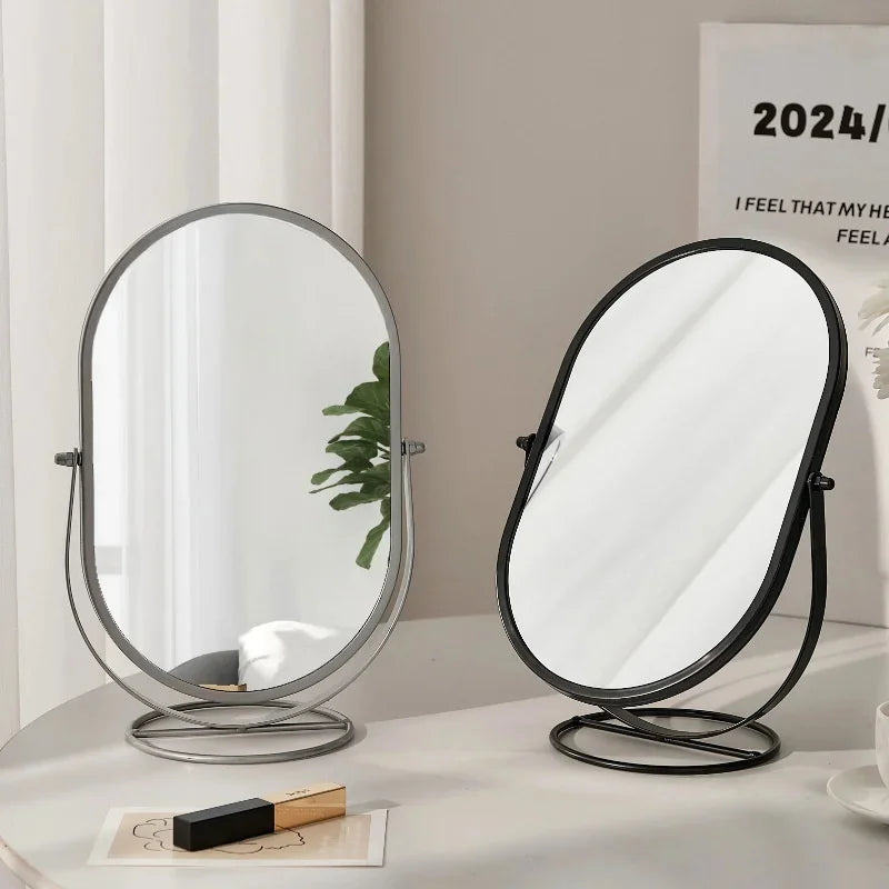A black-framed oval vanity mirror with a silver base sitting on a white surface.