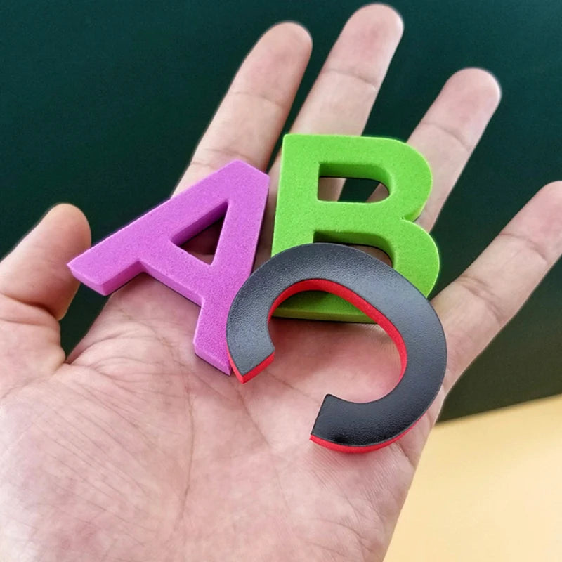 Three magnetic alphabet letters A, B, and C in purple, green, and black are held in a hand.