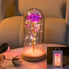 An LED galaxy rose artificial flower displayed inside a glass dome on a white surface.