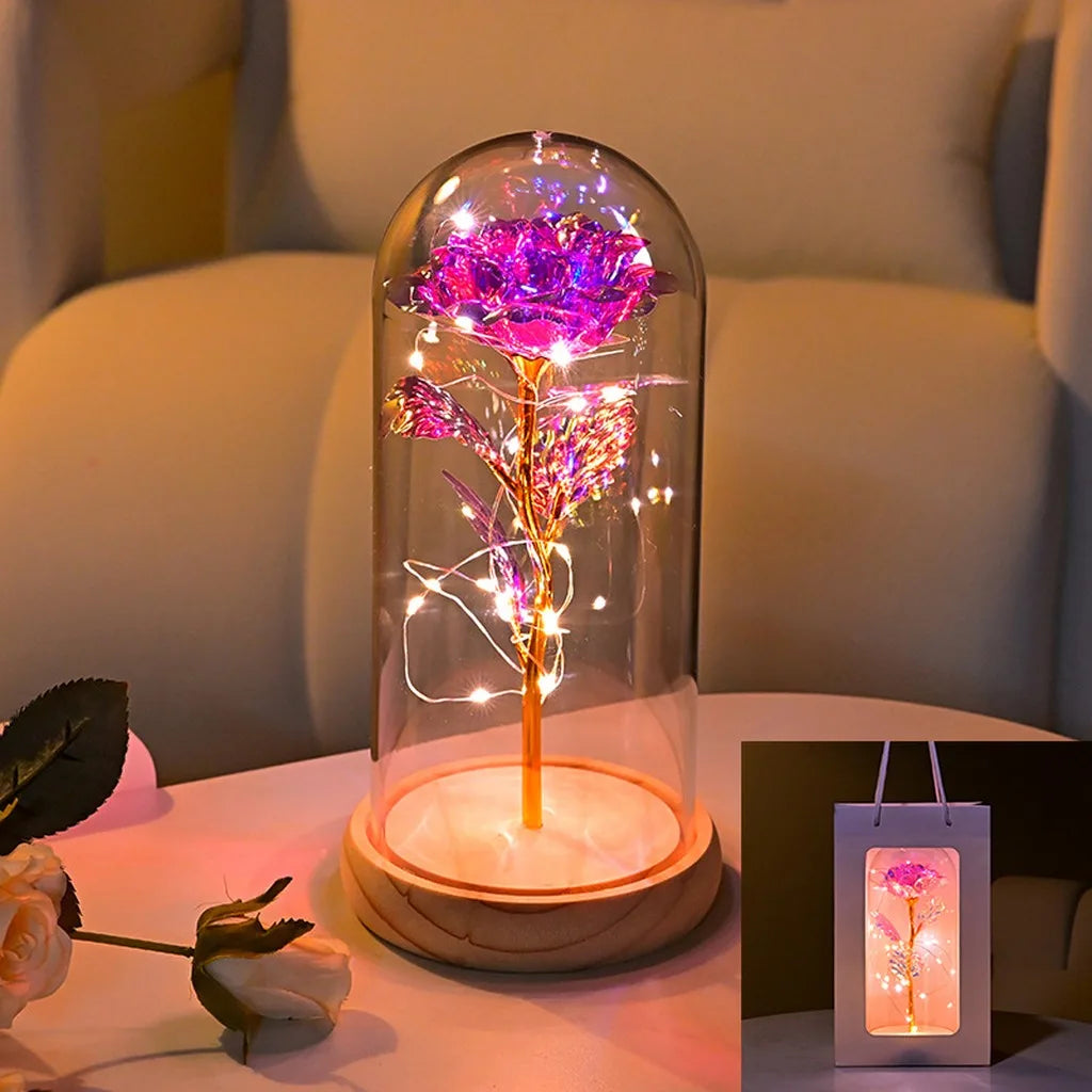 An LED galaxy rose artificial flower displayed inside a glass dome on a white surface.